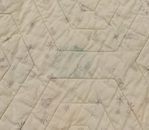Close-up of the back of a quilt. Against a light gray backing, a faded turquoise shape has bled through.