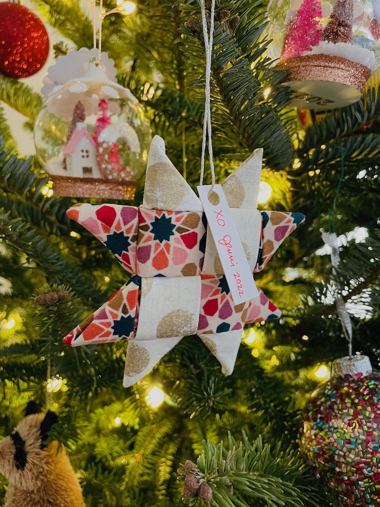 A Scandinavian star folded fabric ornament hangs in a Christmas tree, surrounded by a variety of other ornaments