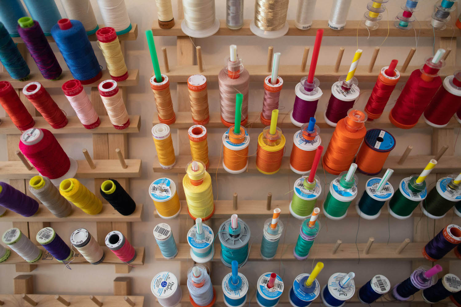 dozens of spools of thread hang on a wall rack in rainbow order