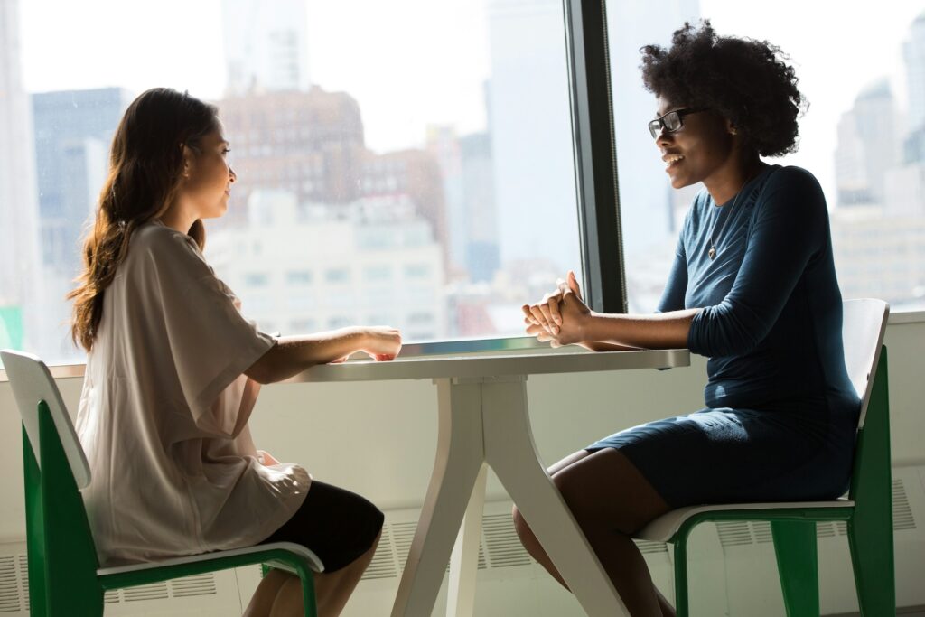 two women sitting at a table together, talking